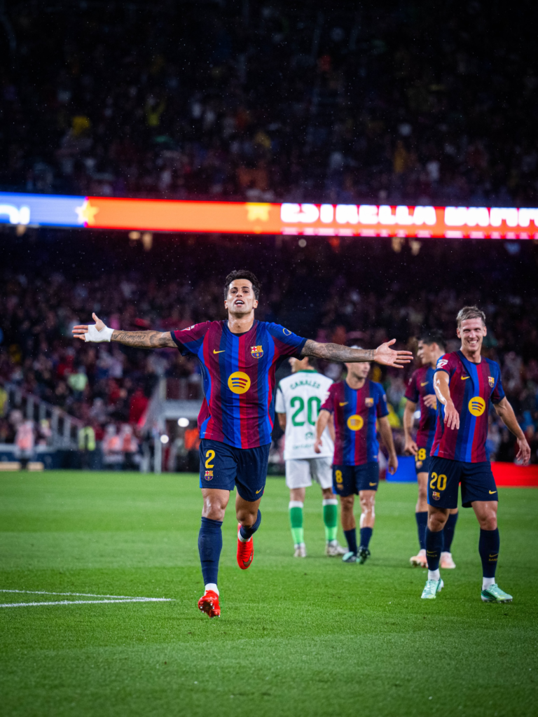 Barcelona defender João Cancelo runs with his arms spread while celebrating his goal against Racing Santander in the rain.