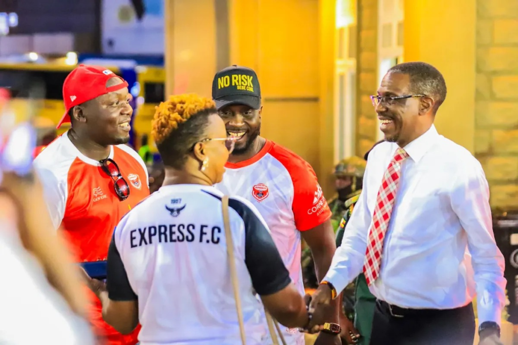 Kiryowa Kiwanuka smiles while speaking with musician Bebe Cool and other Express FC supporters dressed in the club’s red-and-white colours.