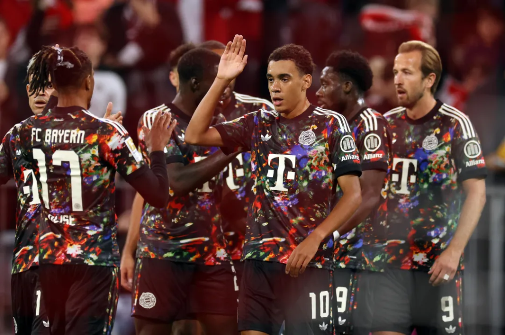 Jamal Musiala of Bayern Munich celebrating his team's first goal with Michael Olise and teammates against Union Berlin.
