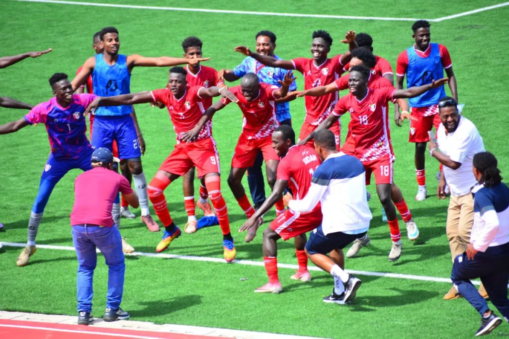 Sudan football players and officials celebrating together on the pitch.