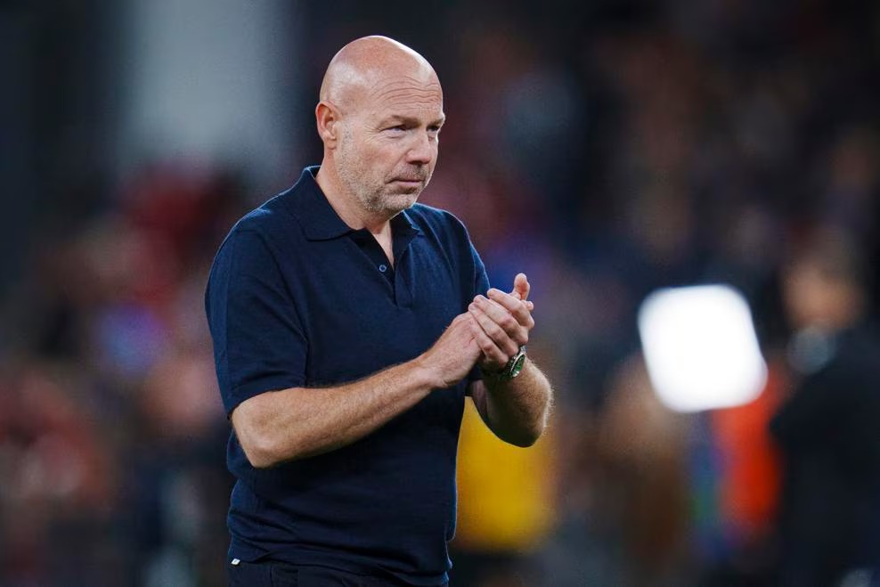 Denmark head coach Brian Riemer applauding on the pitch, wearing a navy polo shirt, before a match.