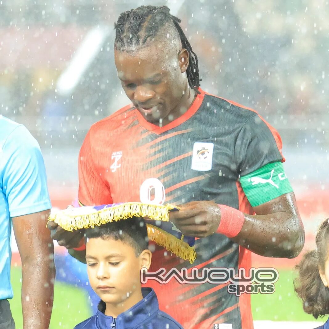 Khalid Aucho shields a young boy from rain.