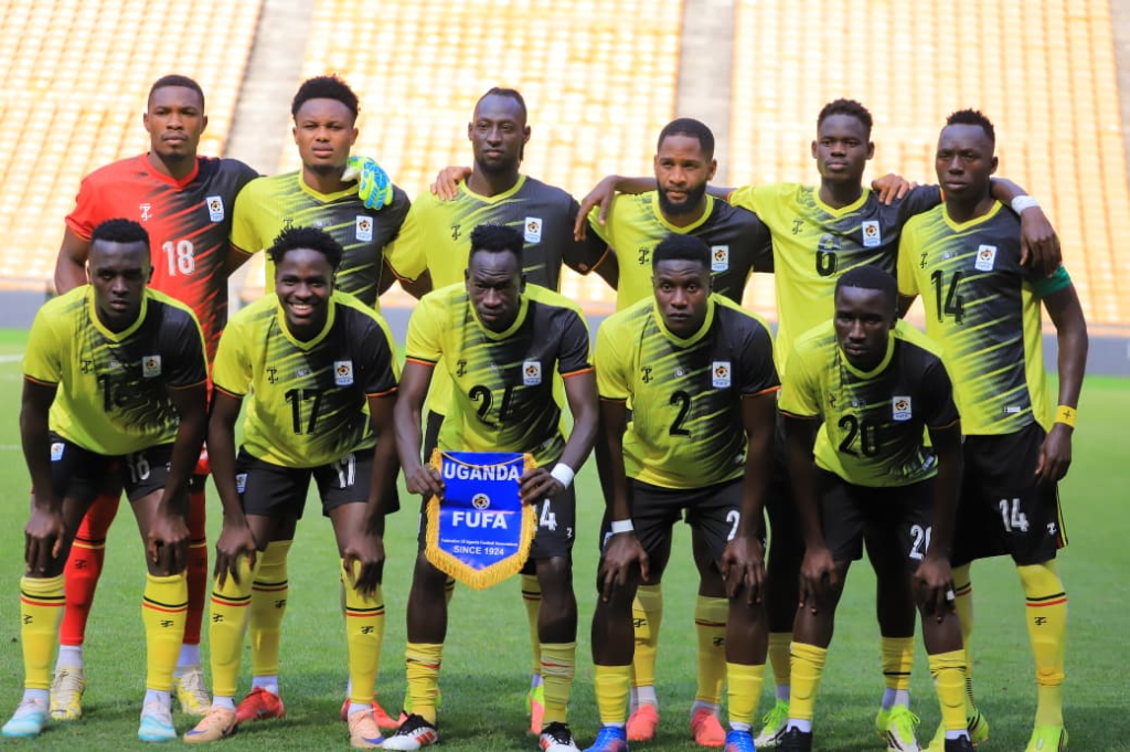 The Uganda Cranes starting XI posing for a team photo, with a player holding a "Uganda FUFA" pennant, ahead of their match against DR Congo.