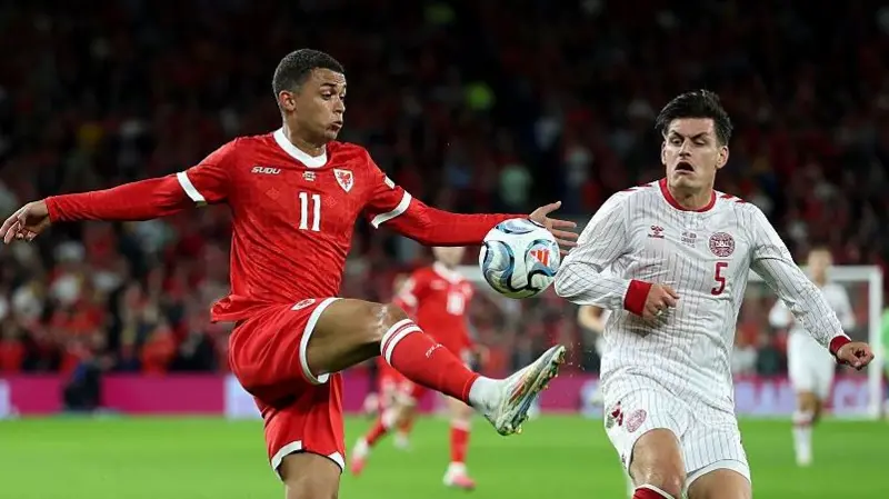 Wales forward Brennan Johnson, wearing No. 11, controlling the ball under pressure from Denmark's No. 5.