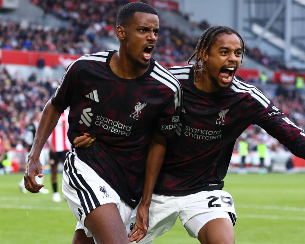 Liverpool’s Alexander Isak, on the left, and Bradley Barcola, wearing No. 29 on the right, celebrating side by side in dark Liverpool kits with their mouths wide open, with a Brentford-style red and white striped player and a blurred crowd behind them.