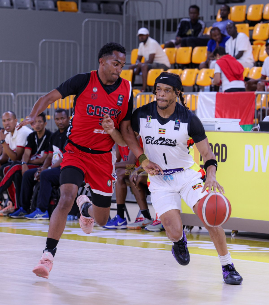 Nam Blazers’ No. 1, in a white Blazers jersey with the Crane Millers logo, a black headband and braids, dribbles the ball with his right hand as a defender in a red and black “Cosep” jersey presses against him. Spectators in yellow seats and bench staff are behind them on a polished court.