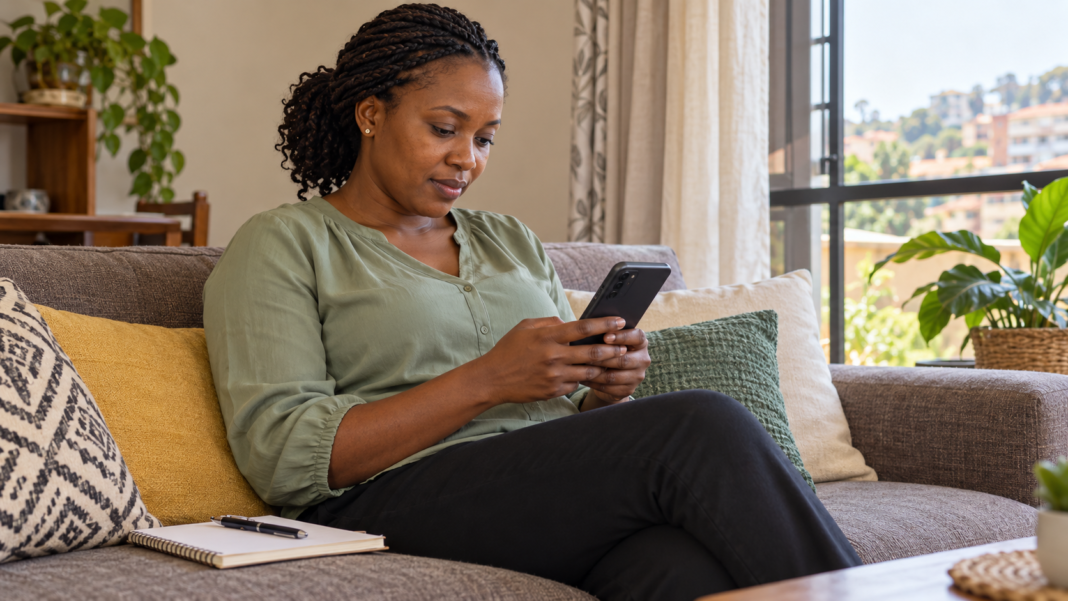 Woman checks her phone beside a notebook at home.